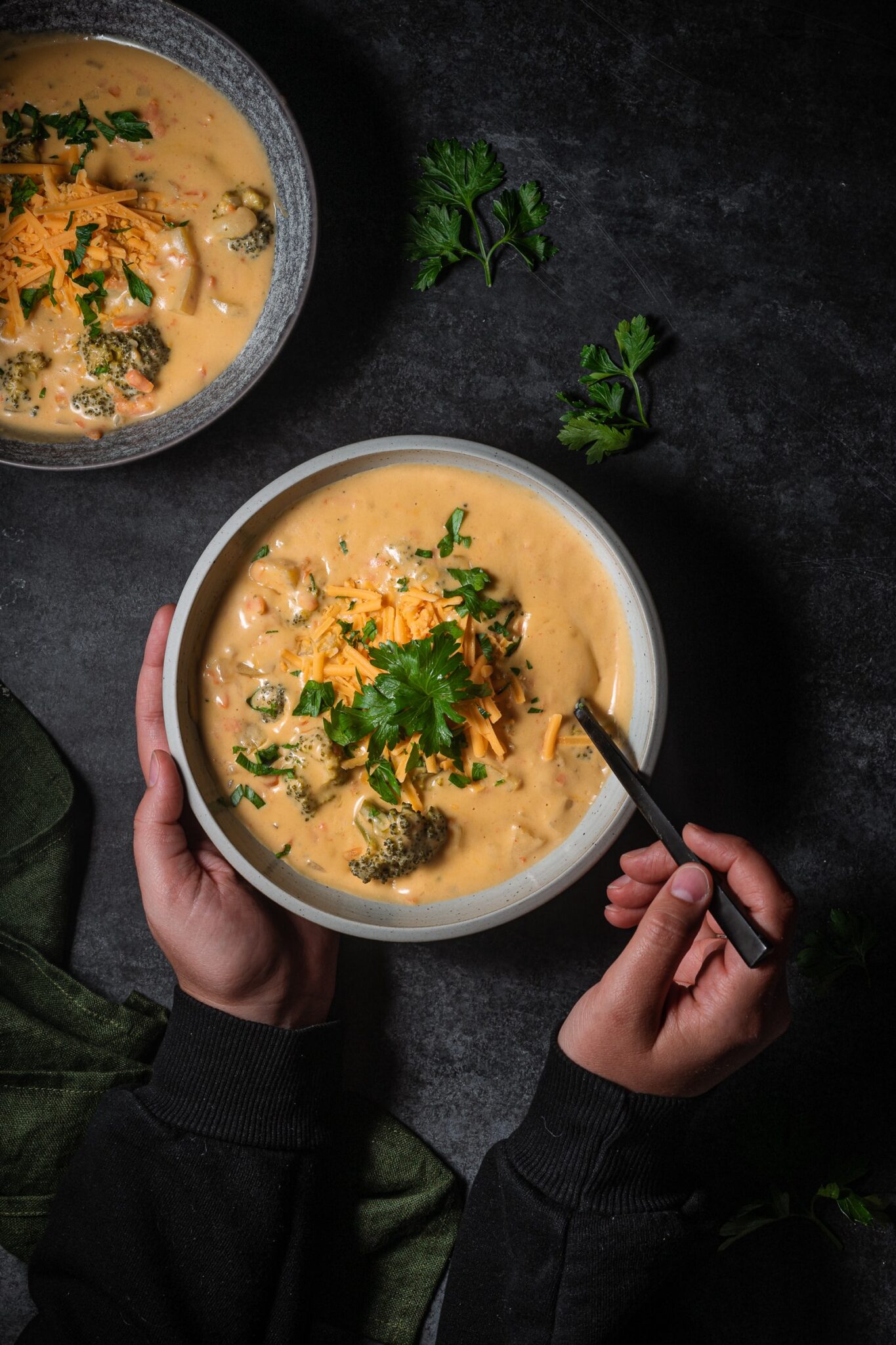 Creamy, vegan broccoli cheddar soup in a shallow bowl topped with vegan cheese and parsley.