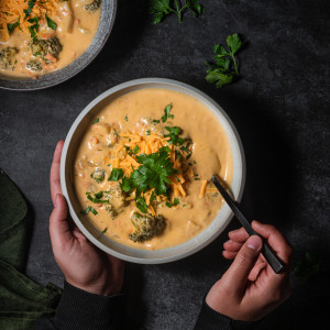 Creamy, vegan broccoli cheddar soup in a shallow bowl topped with vegan cheese and parsley.