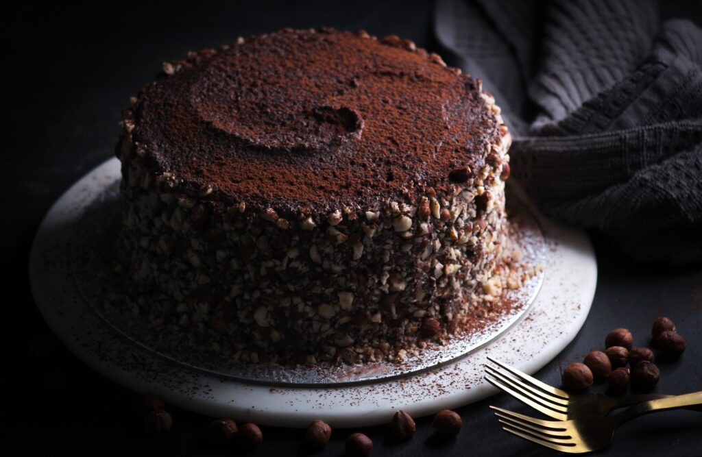 full chocolate cake garnished with cocoa powder and hazelnuts.
