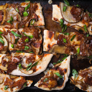 Flatbread on a baking tray topped with tempeh bacon, potato and cheese.