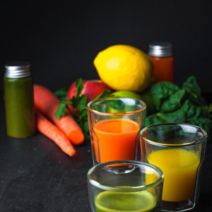 Three different colored Wellness Shots surrounded by fruit and veggies.