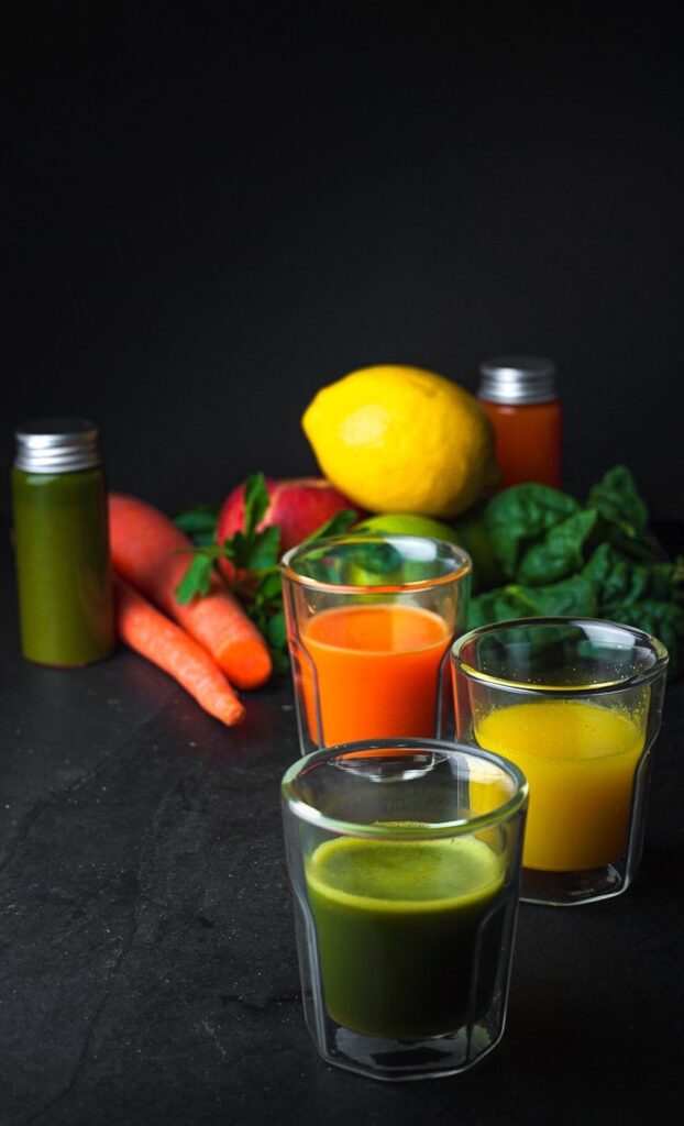 Three different colored Wellness Shots surrounded by fruit and veggies.