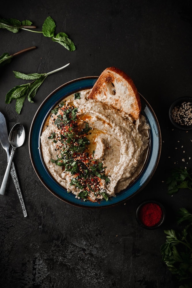 Baba Ganoush served in a shallow bowl with bread and fresh herbs.