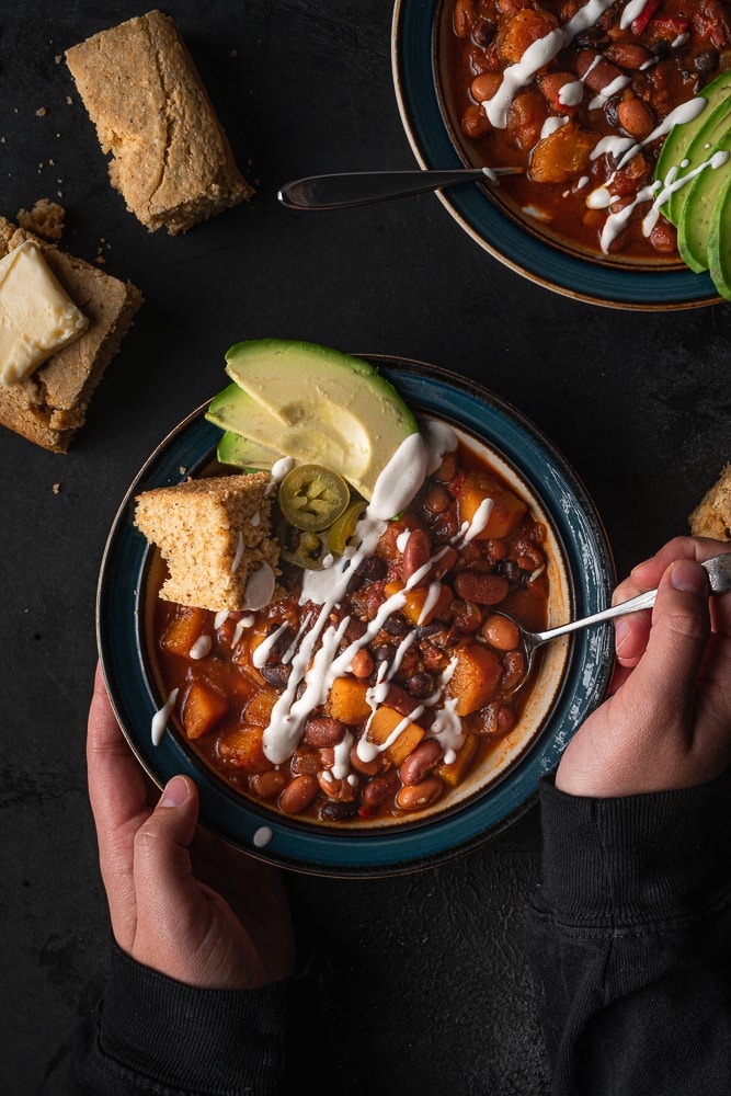 Bowl of chili with avocado and cornbread on top.