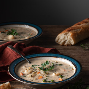 bowl of creamy gnocchi soup with bread and garnished with parsley.
