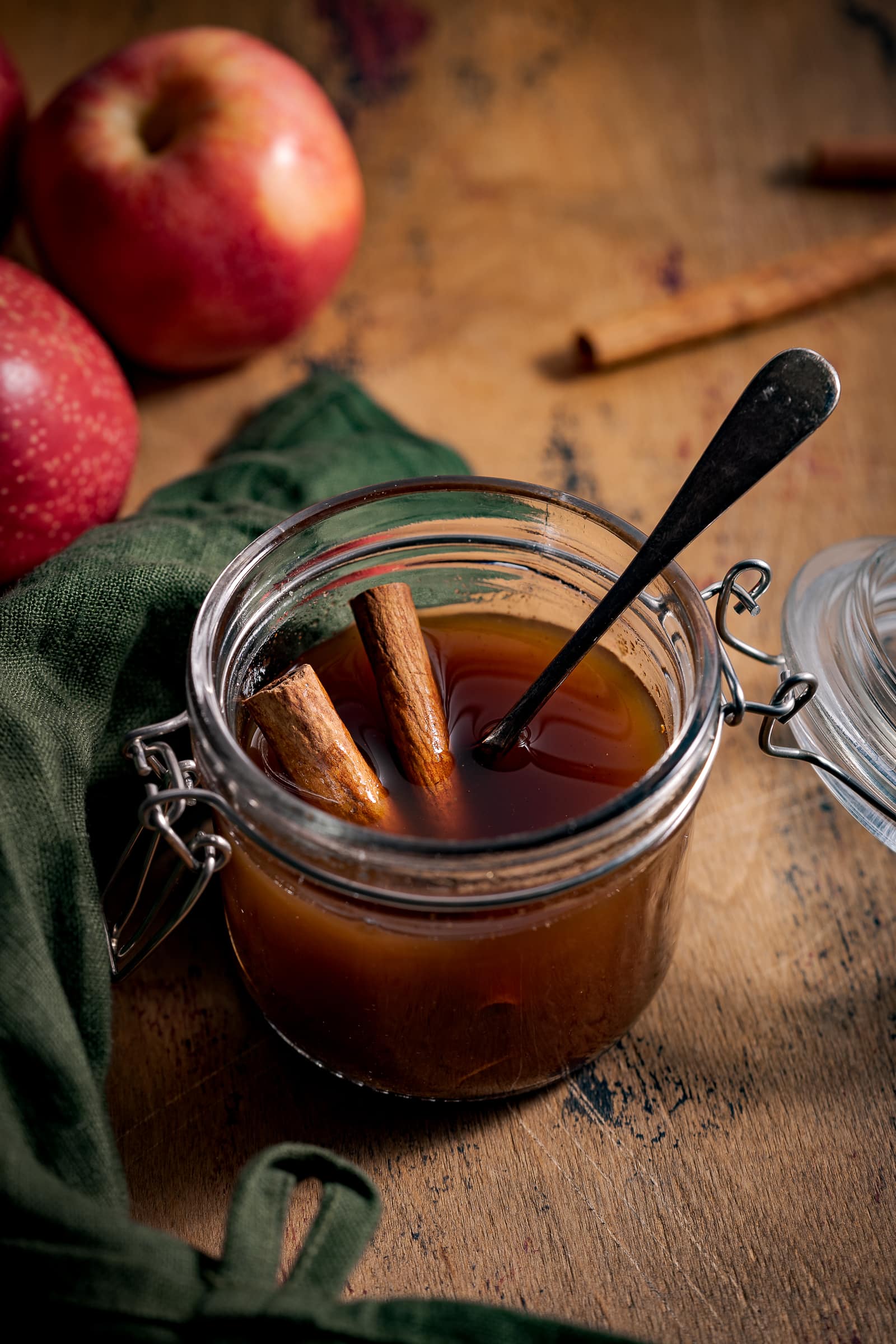 Apple syrup in a small jar with a spoon and cinnamon sticks.