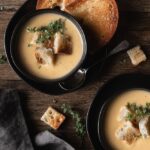 two small bowls of cauliflower leek soup topped with fresh thyme and croutons.
