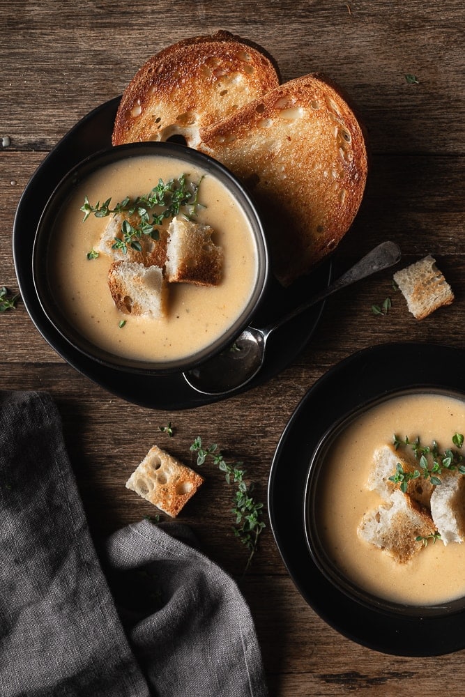 two small bowls of cauliflower leek soup topped with fresh thyme and croutons.