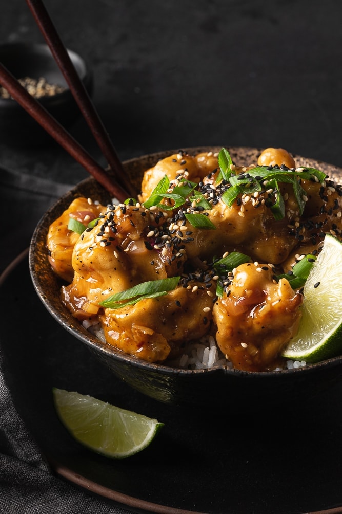 Close up bowl of sesame ginger cauliflower garnished with sesame seeds and green onion. 