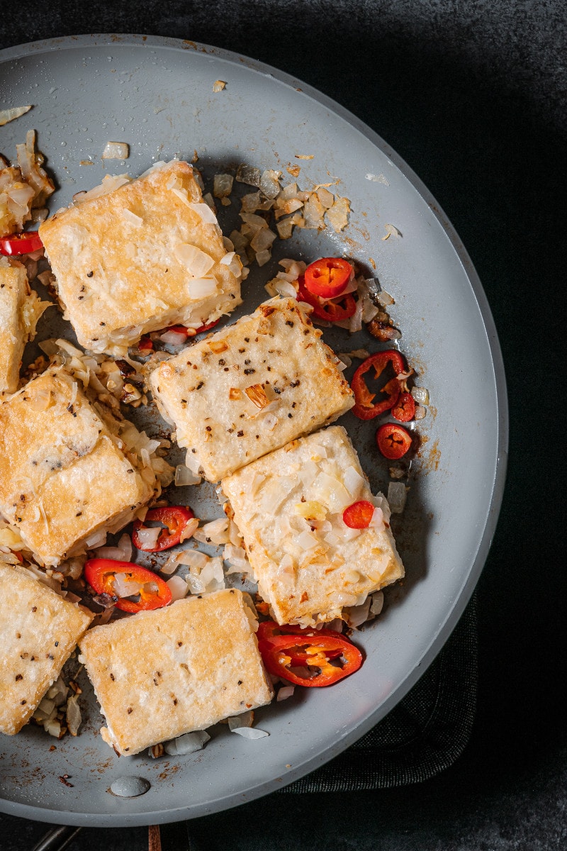 Crispy tofu and onion, garlic, ginger and red chili in frying pan.
