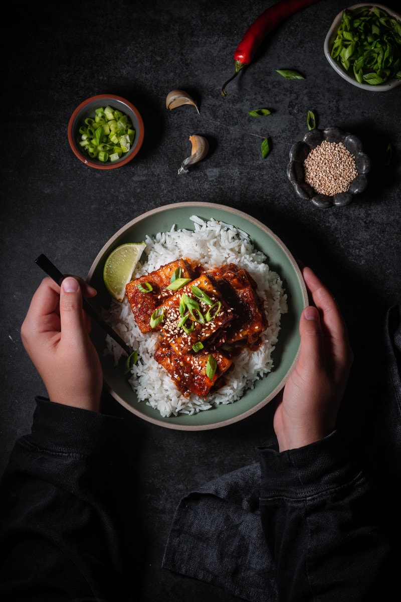 Braised gochujang tofu served over rice garnished with scallions with something grabbing on to the fork.