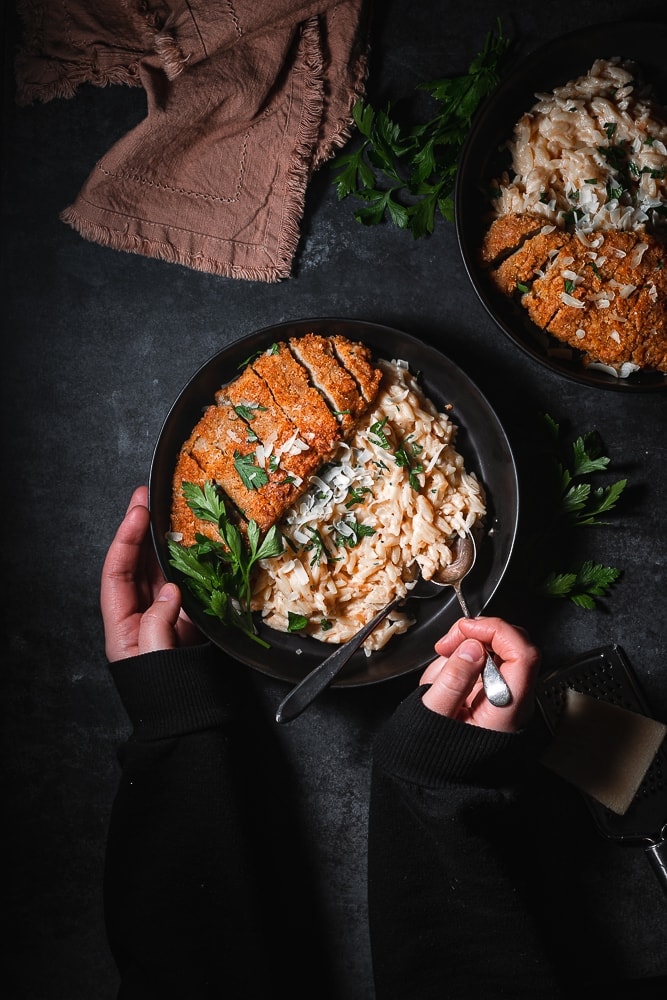 Bowl of Creamy Vegan Garlic Parmesan Orzo paired with crispy vegan chicken and parsley.