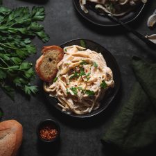 Cashew Cream Sauce Fettuccine Alfredo Served on plates with parsley and garlic bread.