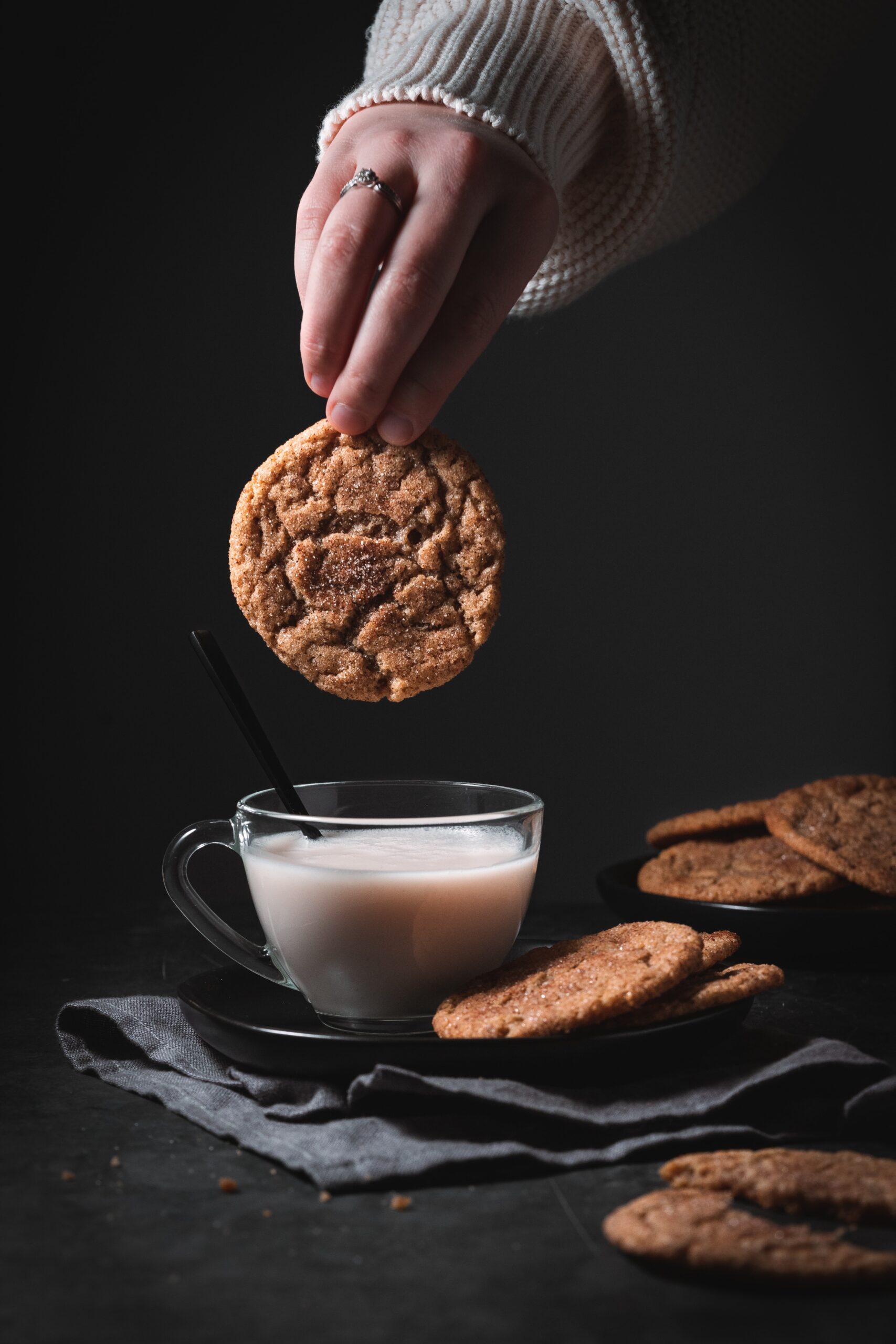 Glass of almond milk surrounded by snickerdoodle cookies with one cookie being dipped in milk.