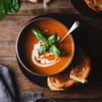 tomato basil soup garnished with basil and grilled cheese on the side