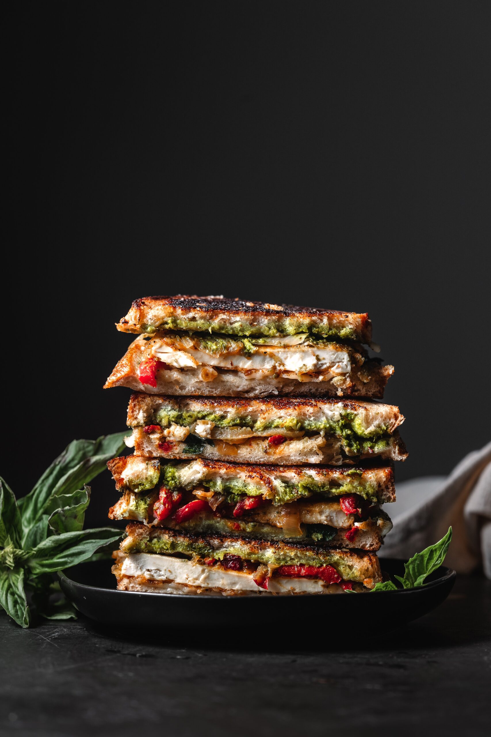 Stack of Tofu Pesto Grilled Cheese Sandwiches garnished with basil.