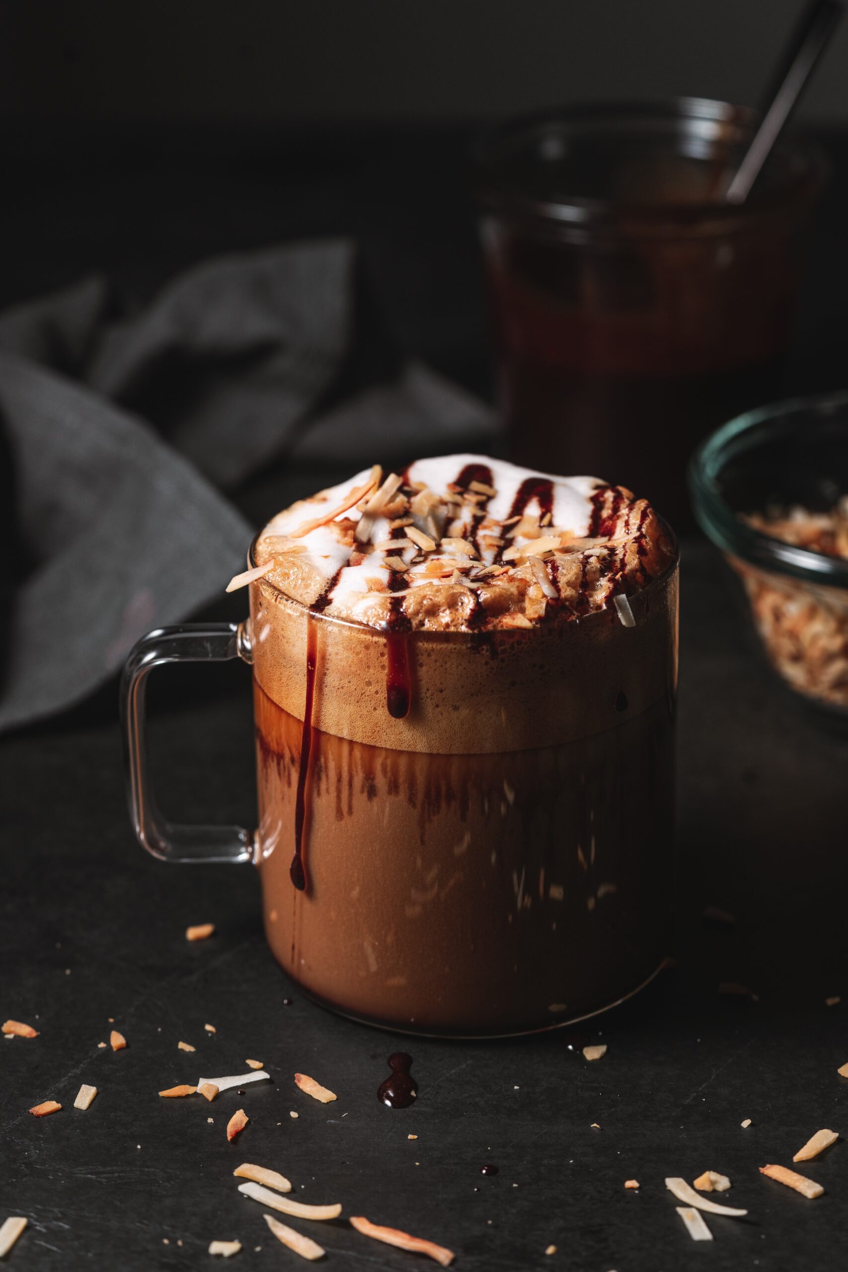 Clear mug filled with a Mocha Latte topped with chocolate syrup drizzle and toasted coconut.