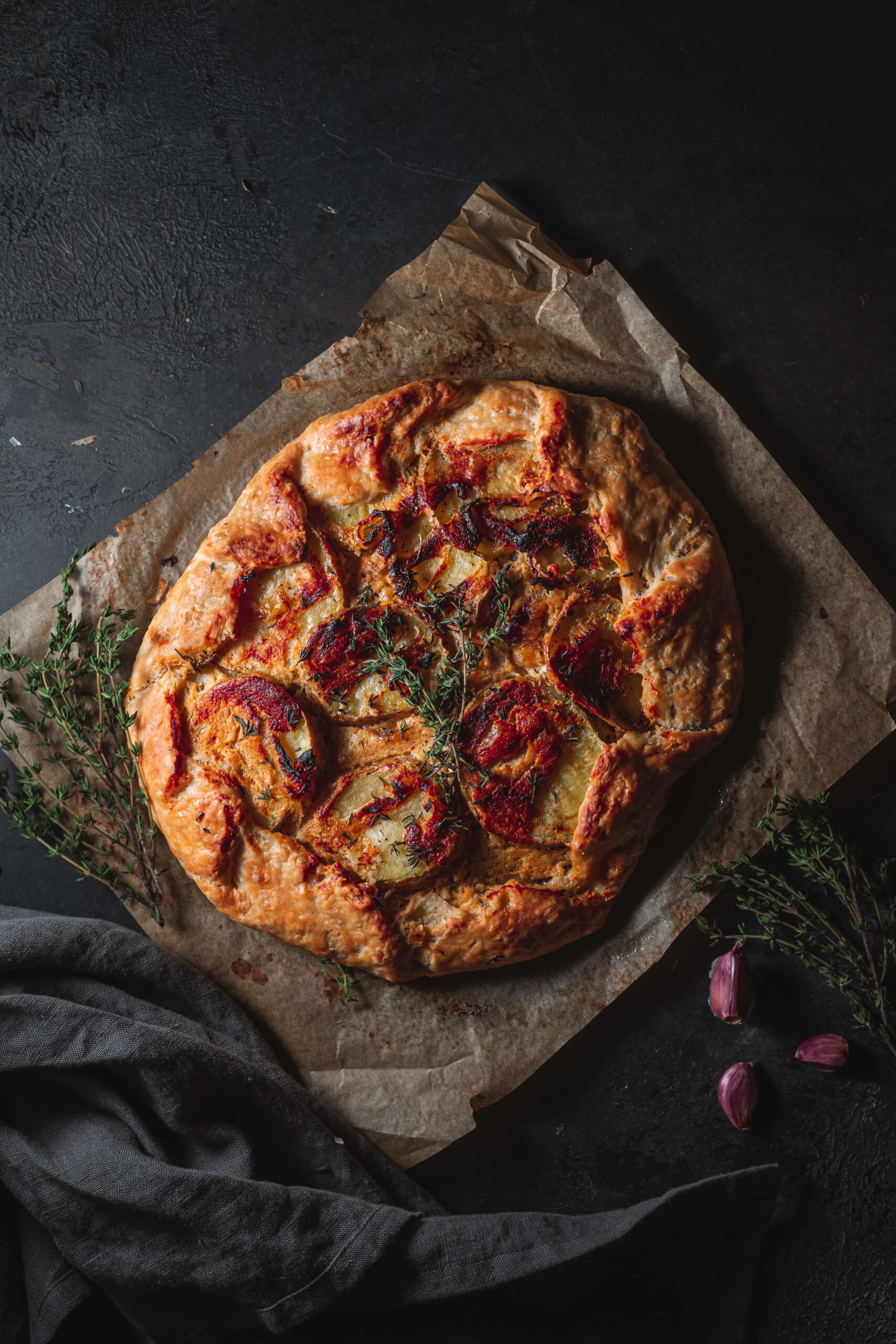 Uncut potato onion galette on parchment paper garnished with fresh thyme.