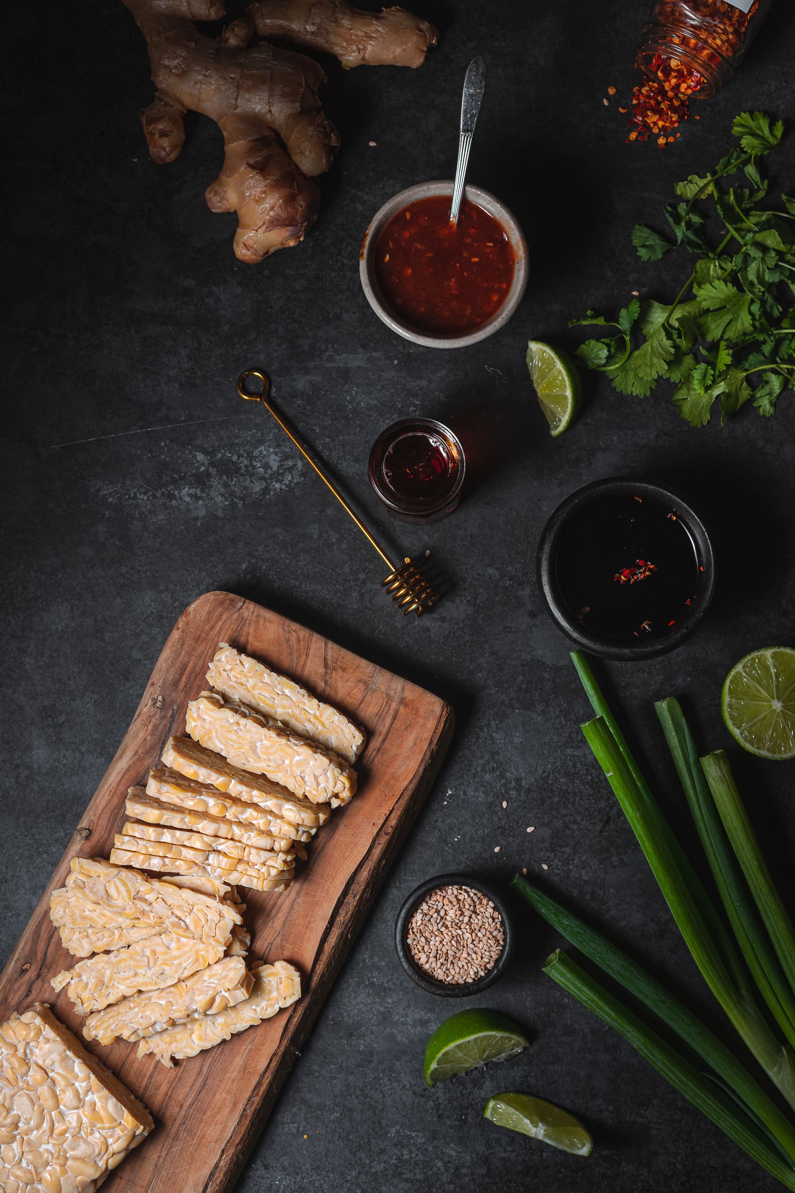 Uncooked Tempeh on cutting board surrounded by popular ingredients found in tempeh dishes.