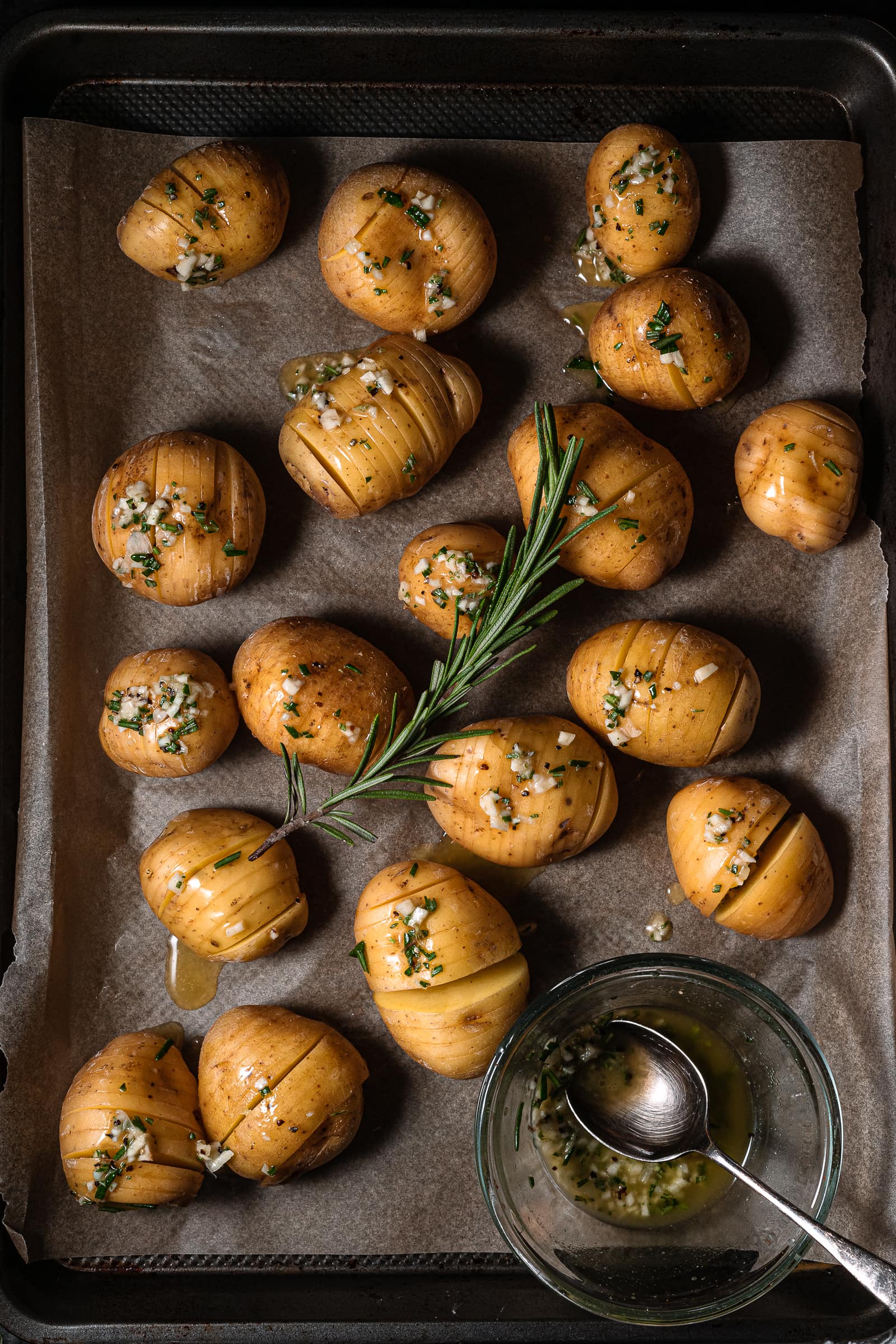 Raw potatoes on tray with garlic butter and rosemary.