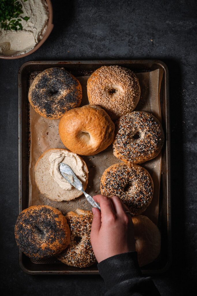 freshly baked bagels on a parchment lined baking tray with cream cheese.