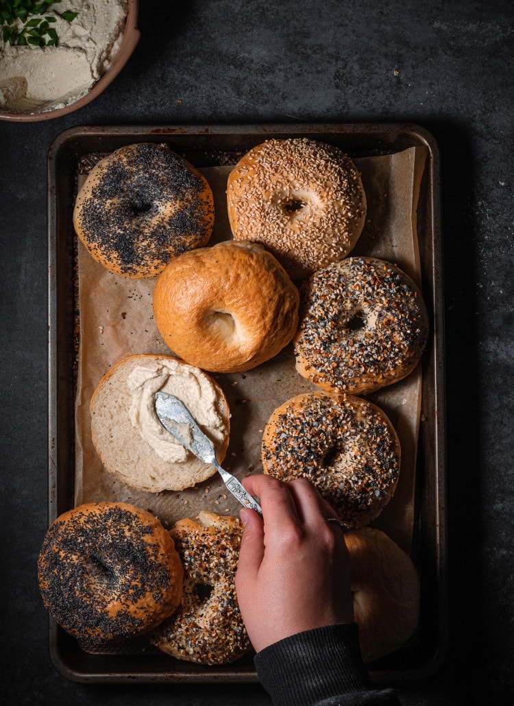 freshly baked bagels on a parchment lined baking tray with cream cheese.