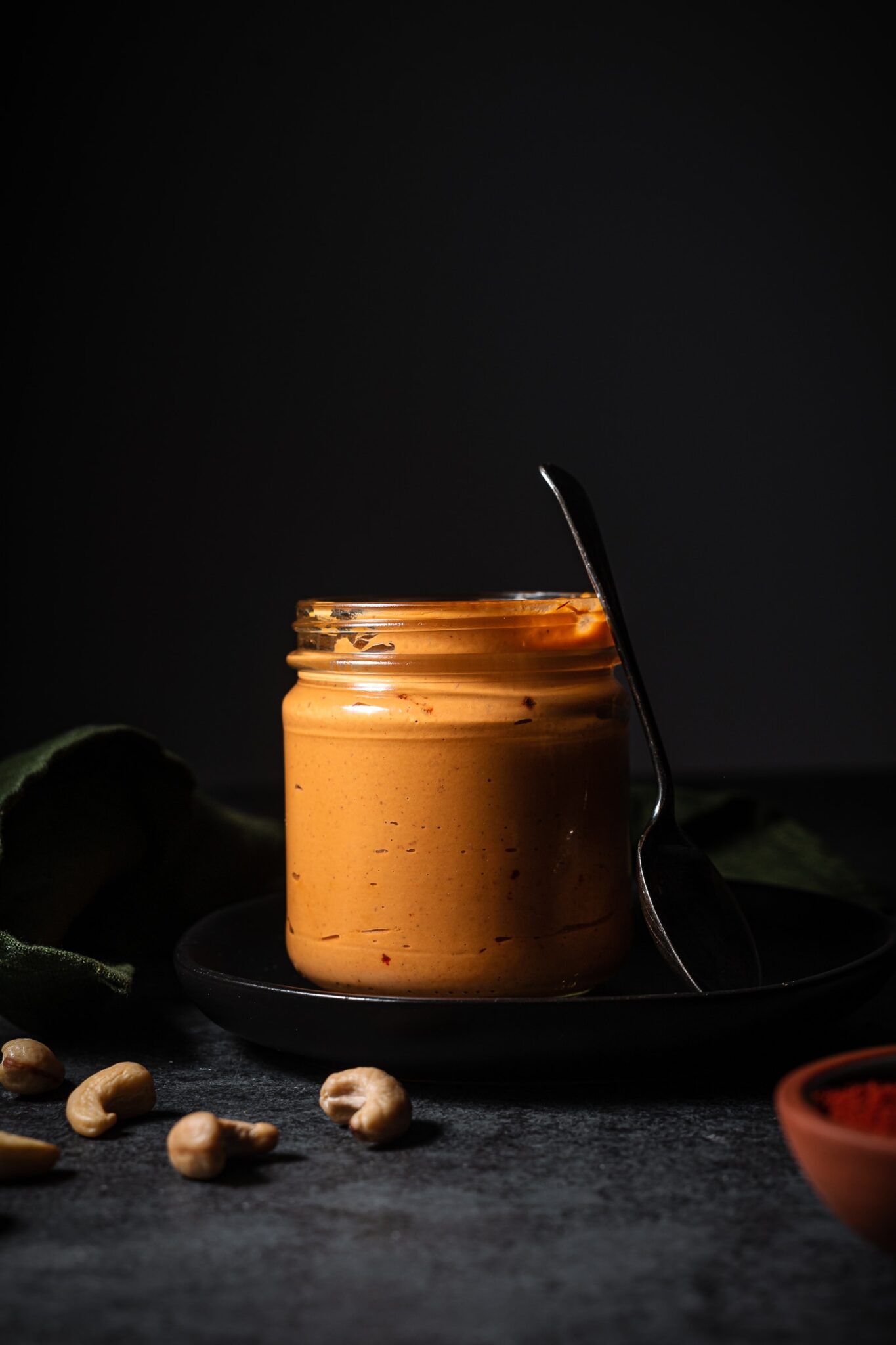 Chipotle aioli jar sitting on a plate with cashews around it.