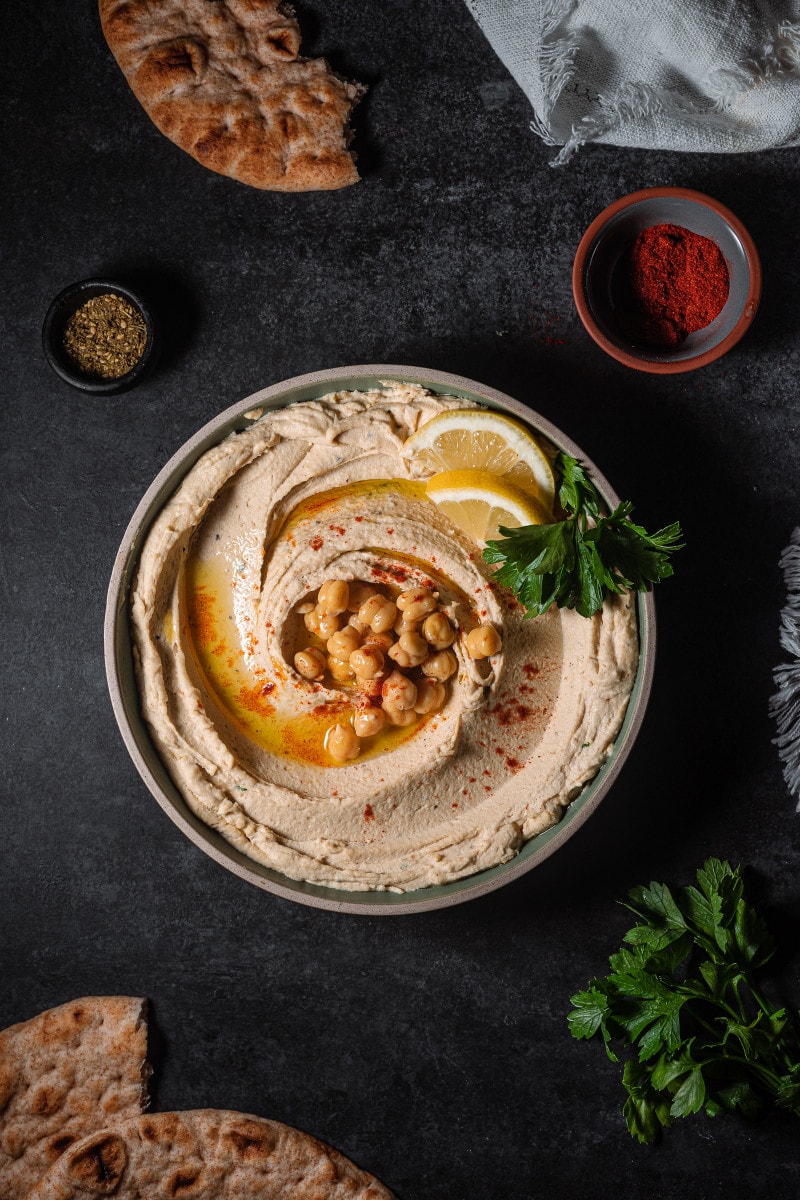Hummus swirled on to a plate topped with chickpeas, parsley and olive oil.