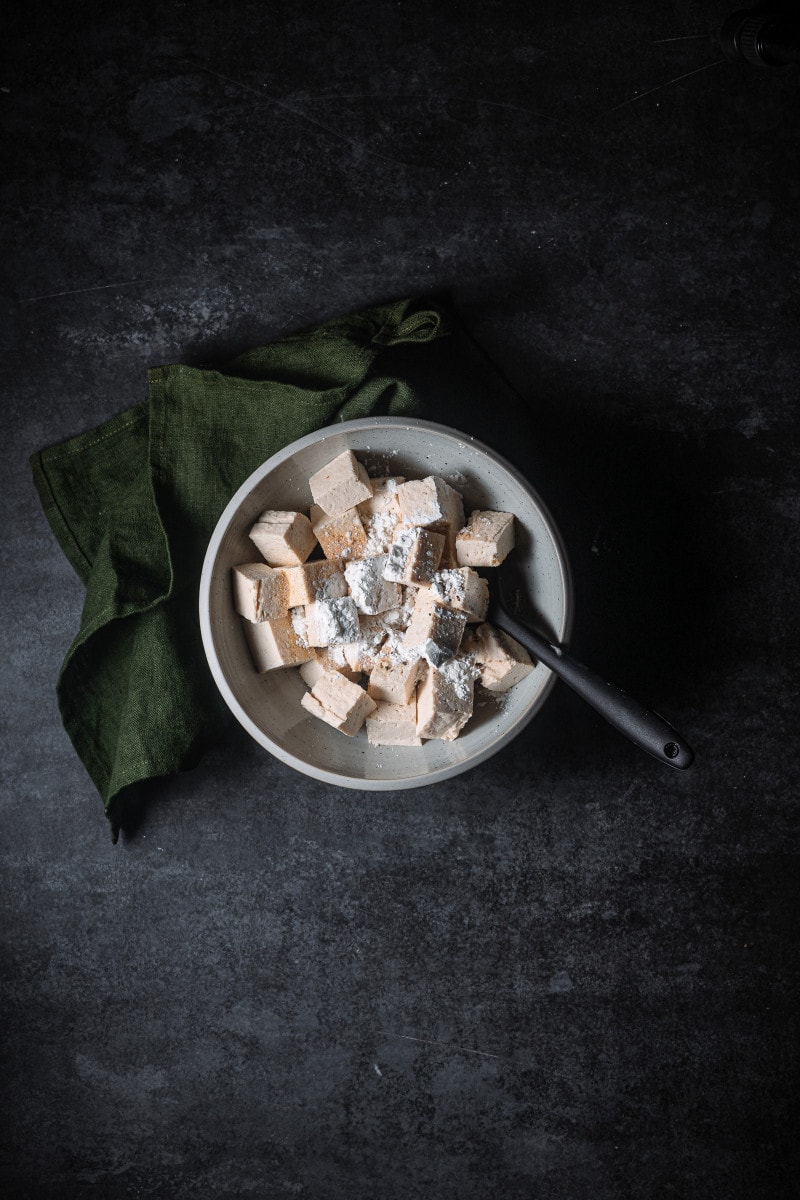 Tofu in a bowl with cornstarch and seasonings.