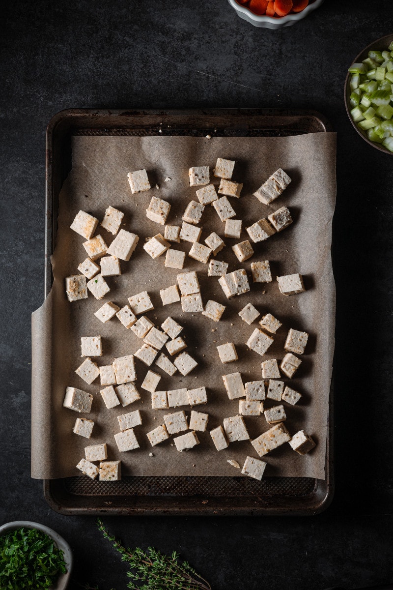 Tofu that is cubed and tossed in spices on a baking tray.