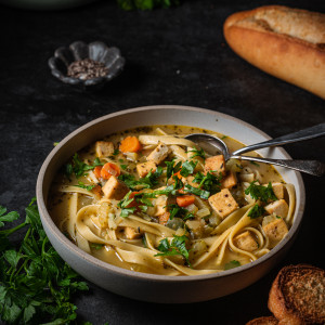 A serving of vegan chicken noodle soup in a serving bowl with bread.