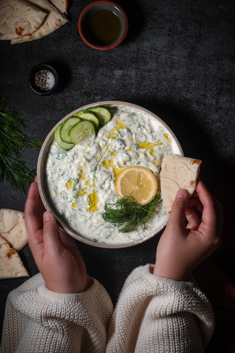 Homemade tzatziki sauce in a serving dish with flatbread and cucumbers.