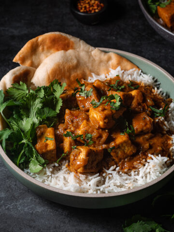 Butter tofu in a bowl over rice with cilantro and naan.