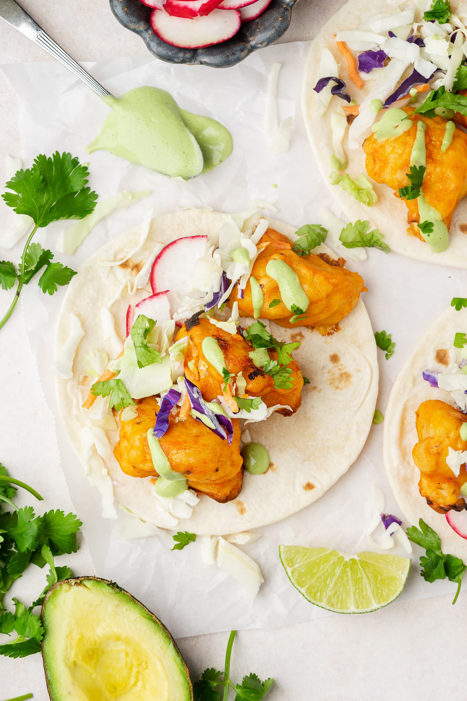 Buffalo cauliflower tacos topped with cilantro lime sauce, mixed cabbage, and radishes.