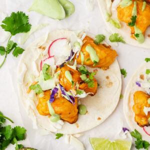 Buffalo cauliflower tacos topped with cilantro lime sauce, mixed cabbage, and radishes.