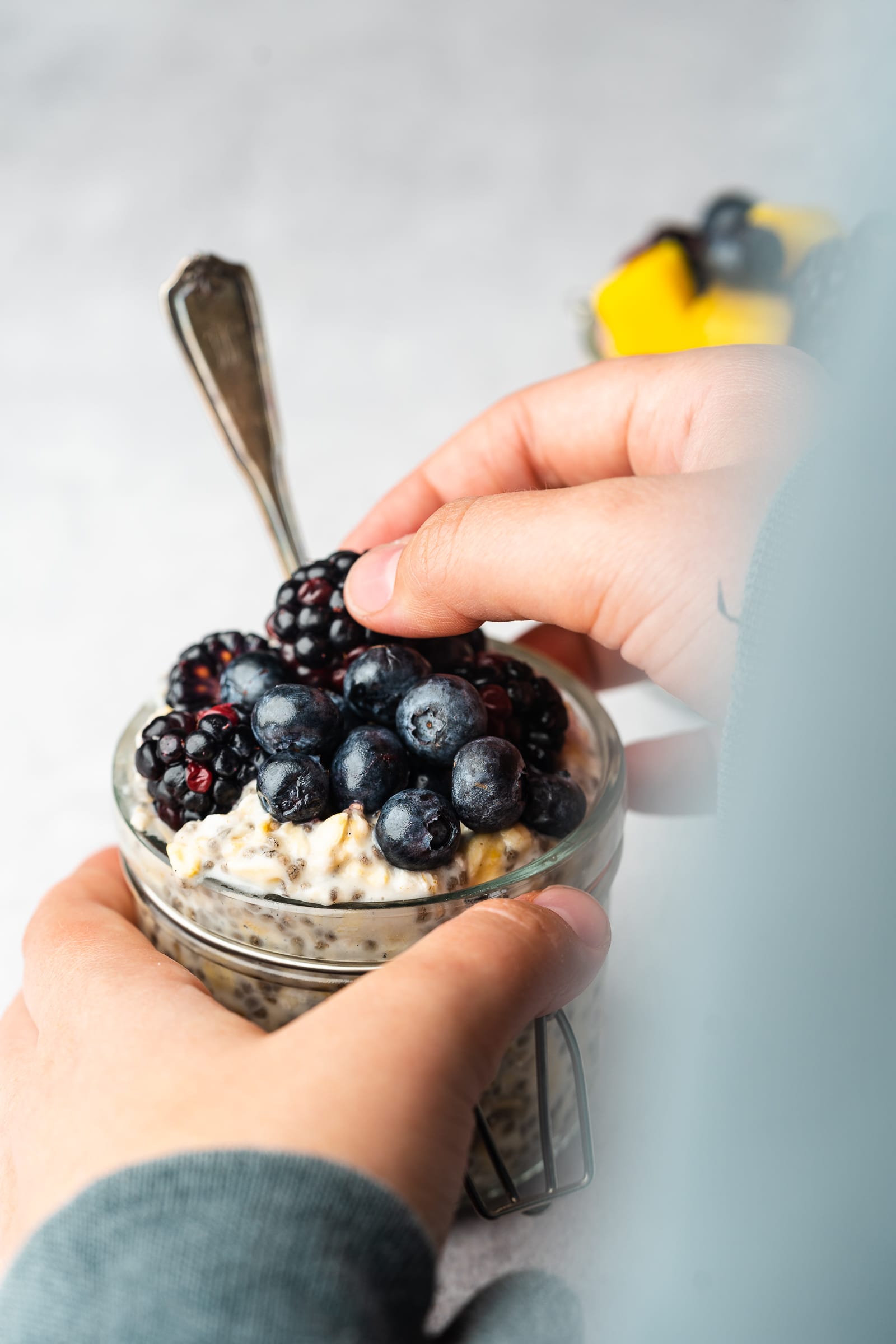 Small glass jar of almond milk overnight oats and blueberries and blackberries being placed on top.