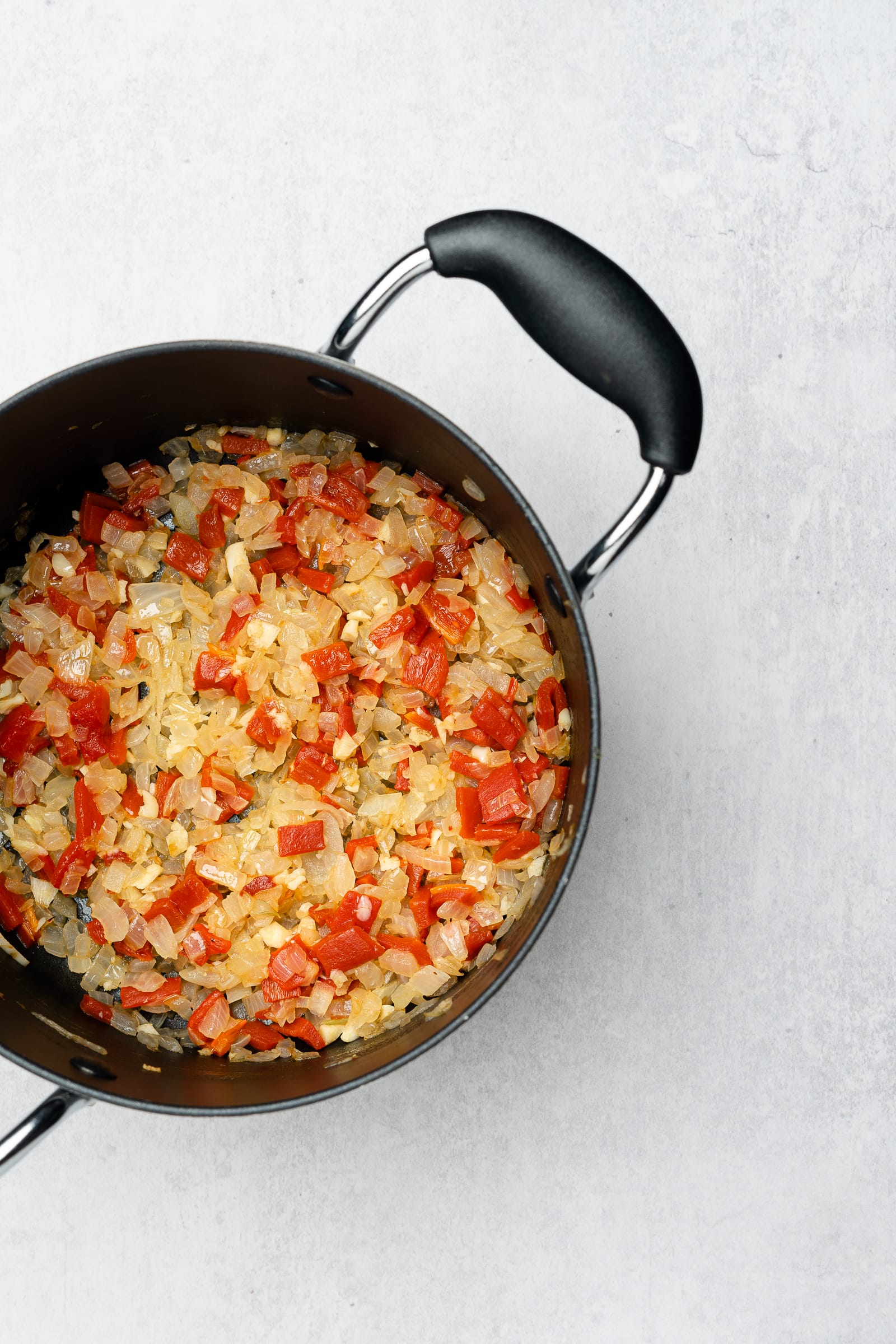 Soup pot with cooked onions and red bell peppers.