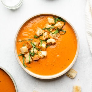 Bowl of tomato basil soup with croutons and basil.