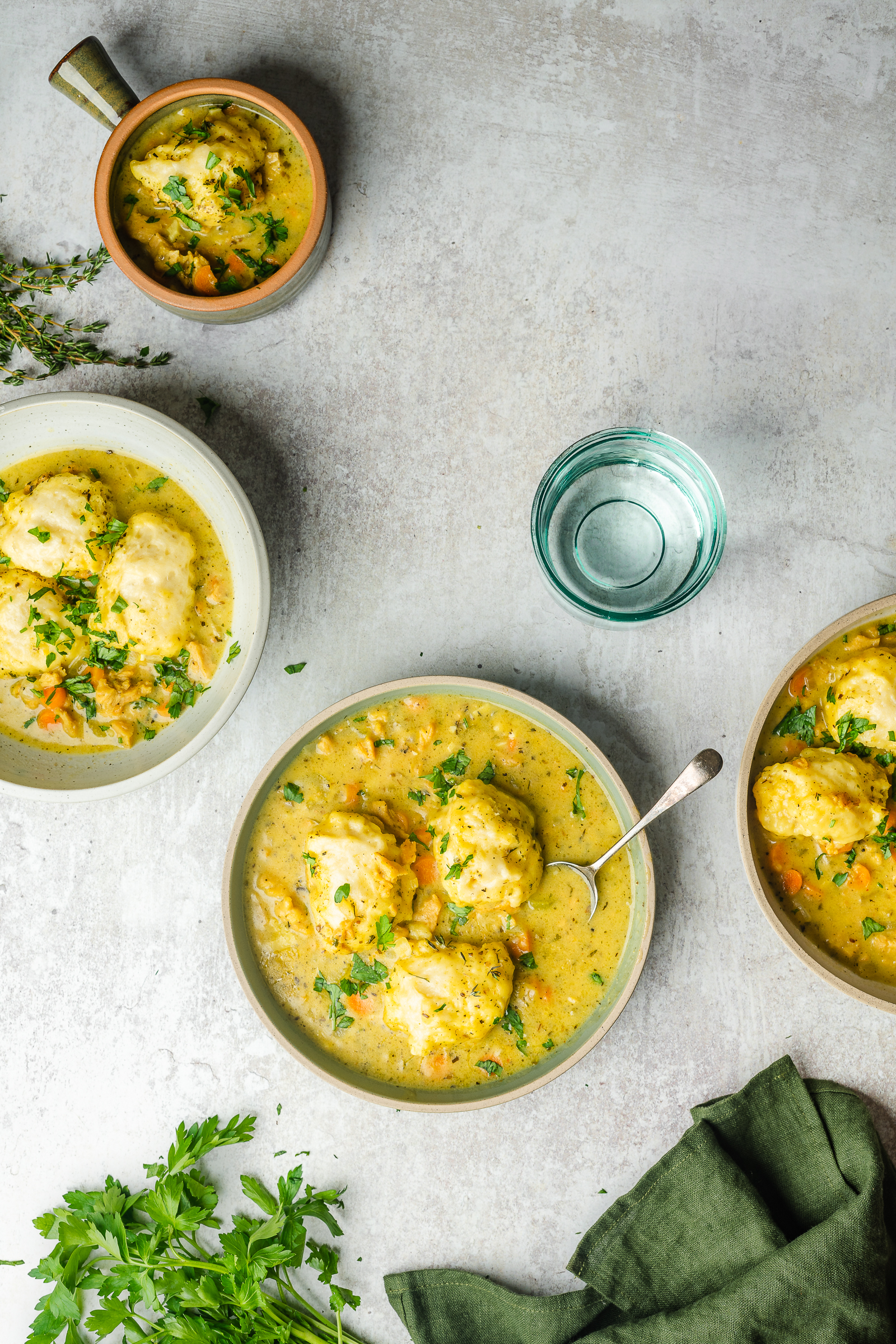 4 bowls of chicken and dumplings in serving dishes garnished with parsley.