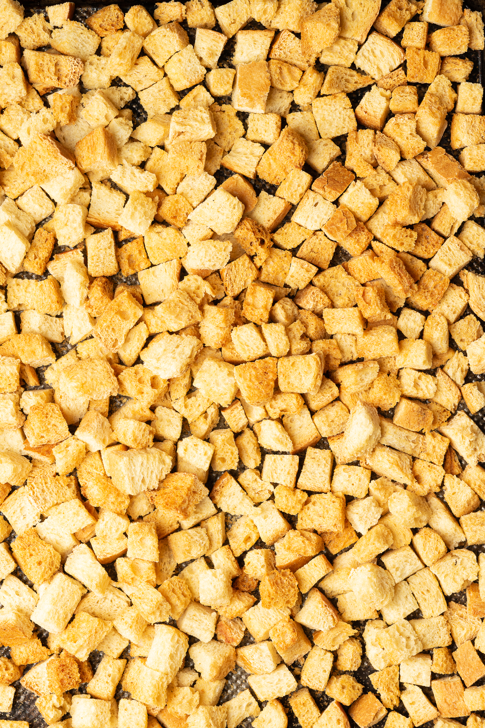 Dried crispy bread cubes on a baking tray.