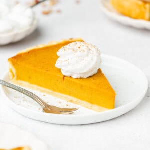 Pumpkin pie slice on small serving plate with dollop of whipped cream and cinnamon.