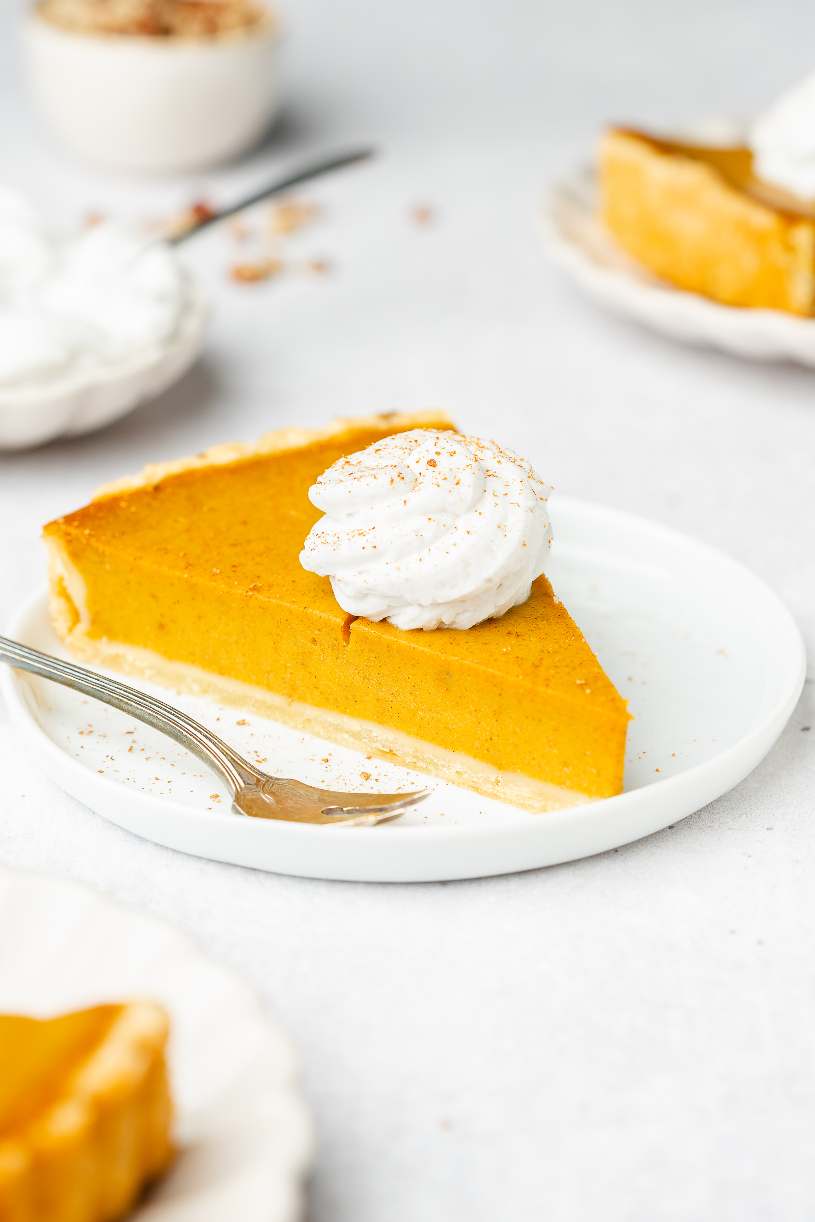 Pumpkin pie slice on small serving plate with dollop of whipped cream and cinnamon.