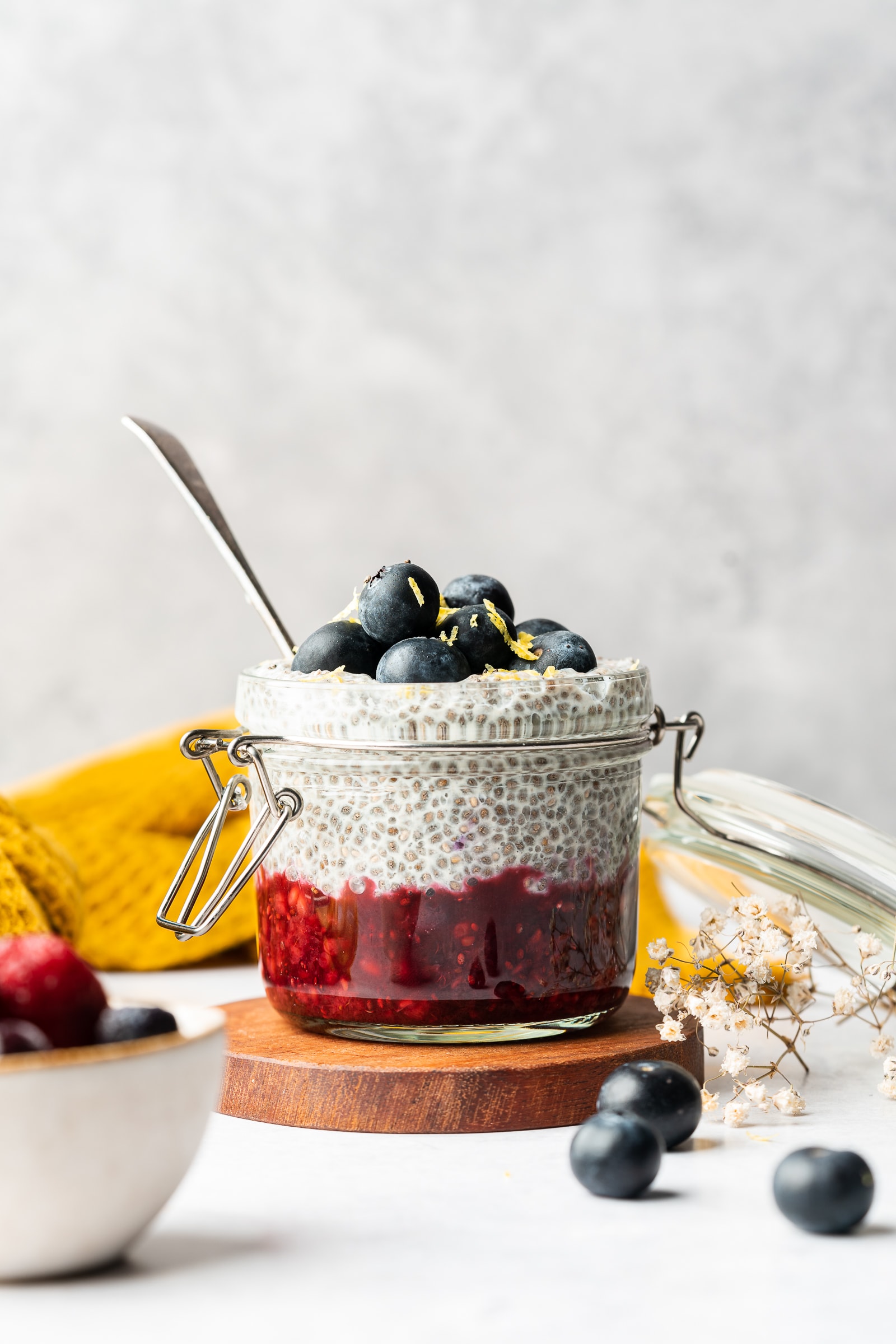 Chia pudding made with oat milk in a glass jar layered with fresh blueberries and berry jam.