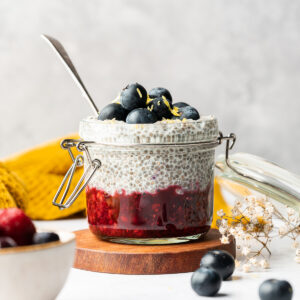 Chia pudding made with oat milk in a glass jar layered with fresh blueberries and berry jam.