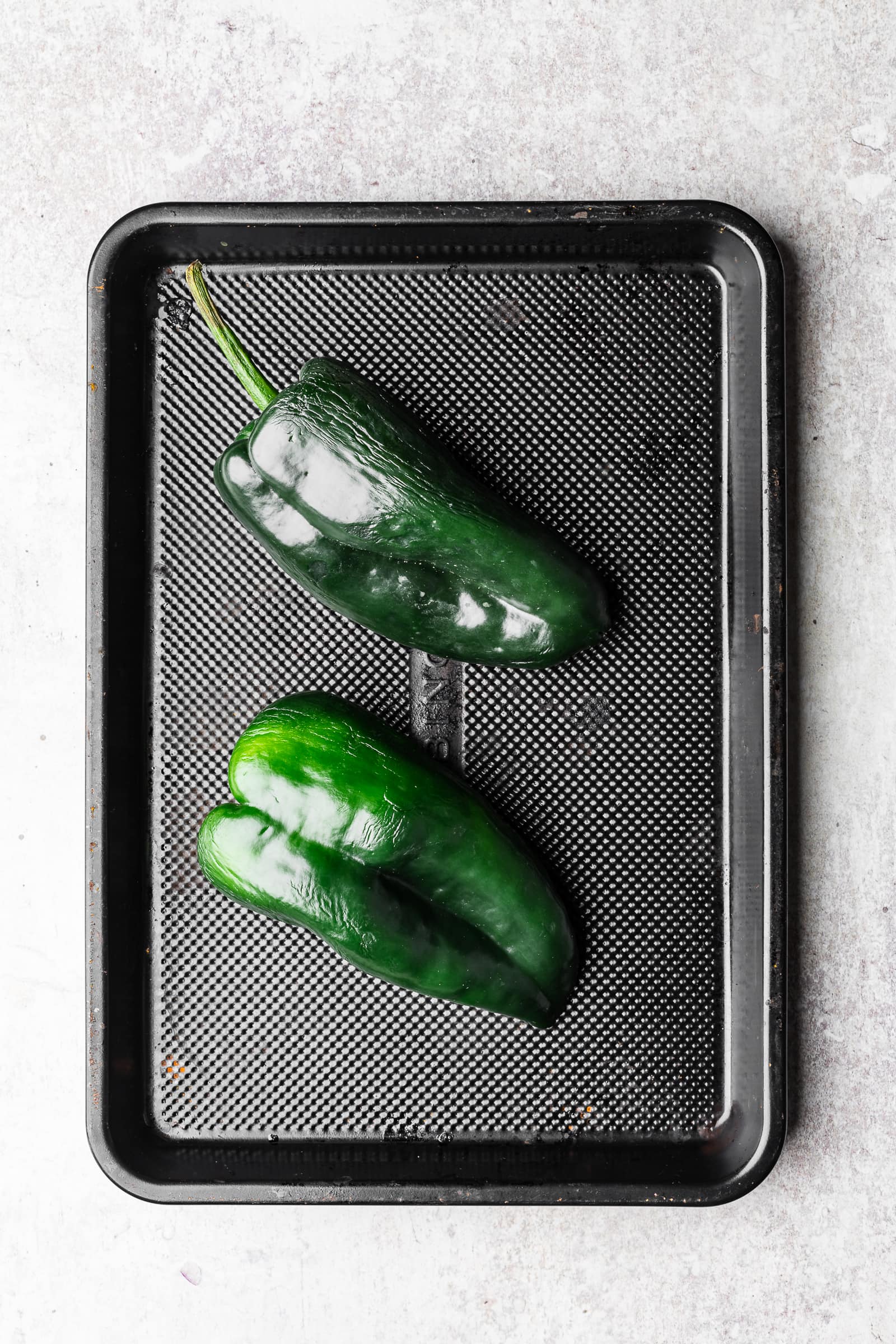 Poblano peppers on a black baking pan.