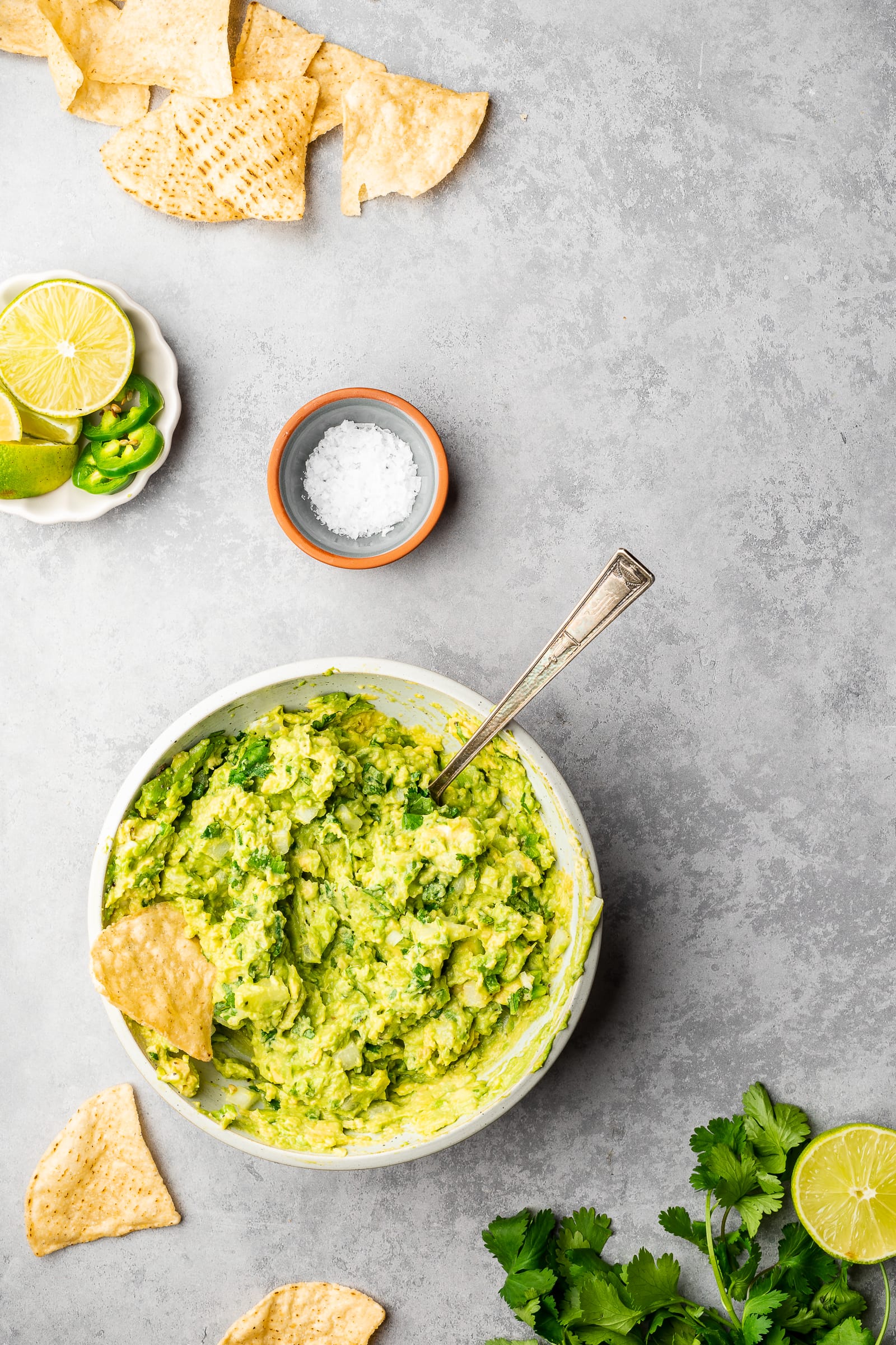 Fresh guacamole without tomatoes in a shallow bowl surrounded by chips.