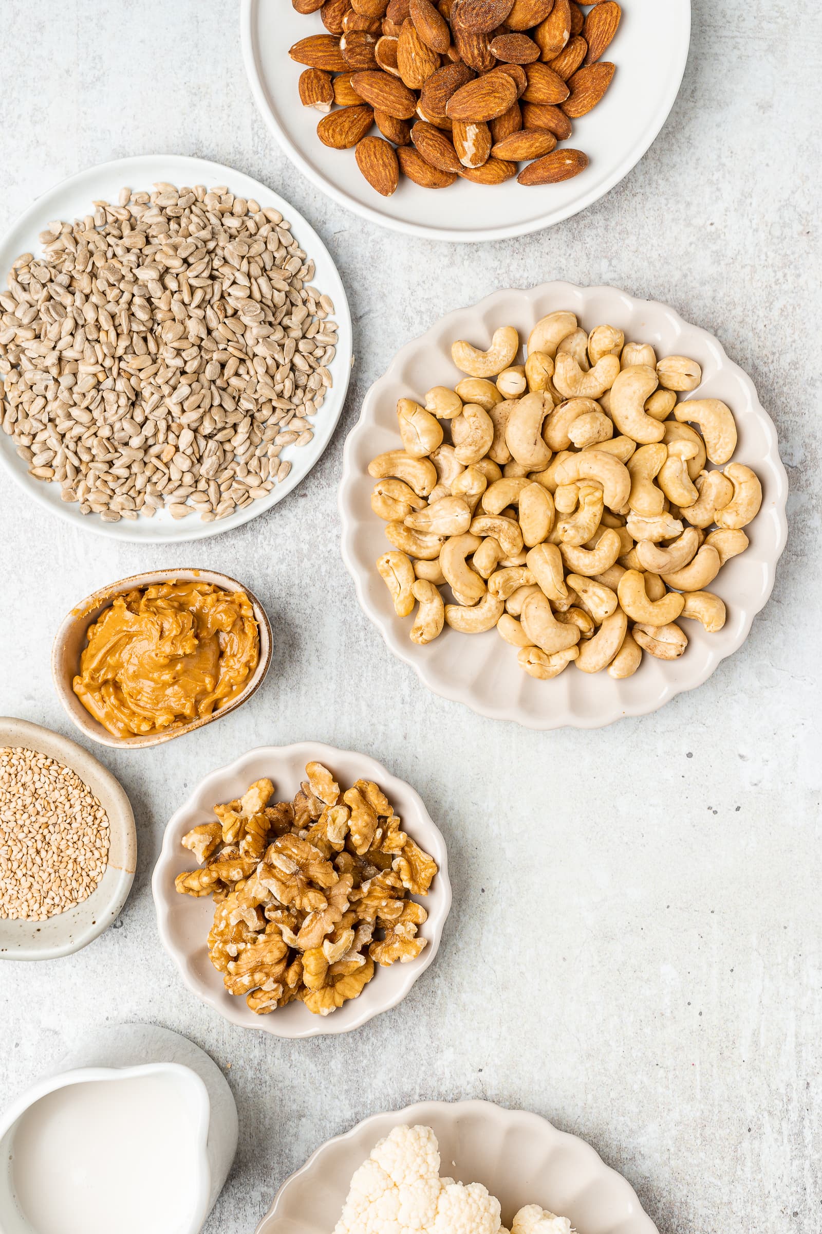 Variety of nuts, seeds, cauliflower, and peanut butter on small serving plates.