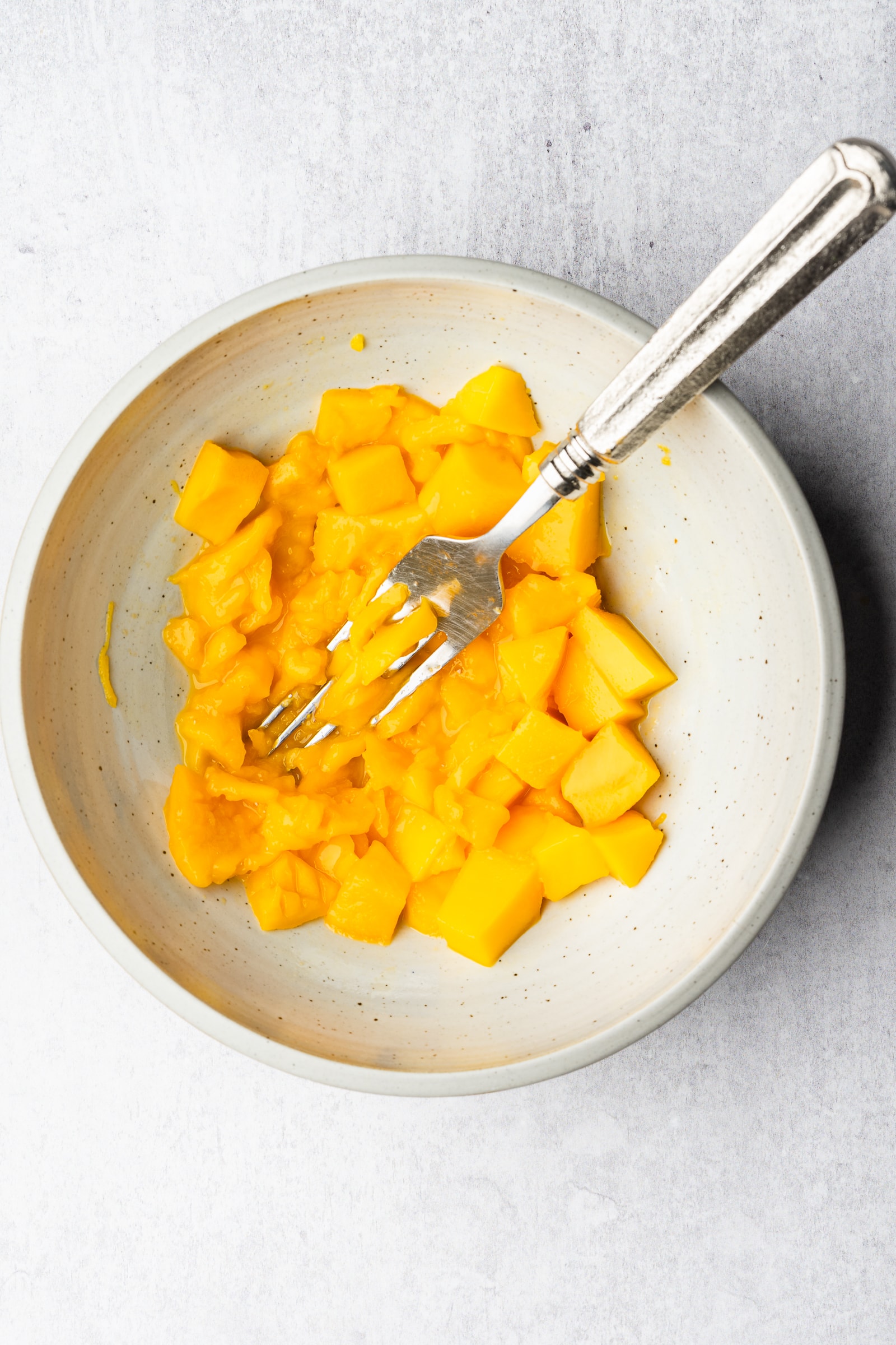 Ripe mango being mashed in bowl.