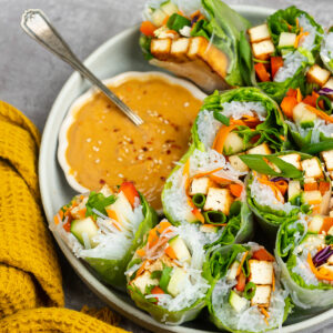 Fresh spring rolls cut in half and placed cut side up in a shallow bowl with peanut sauce on the side.