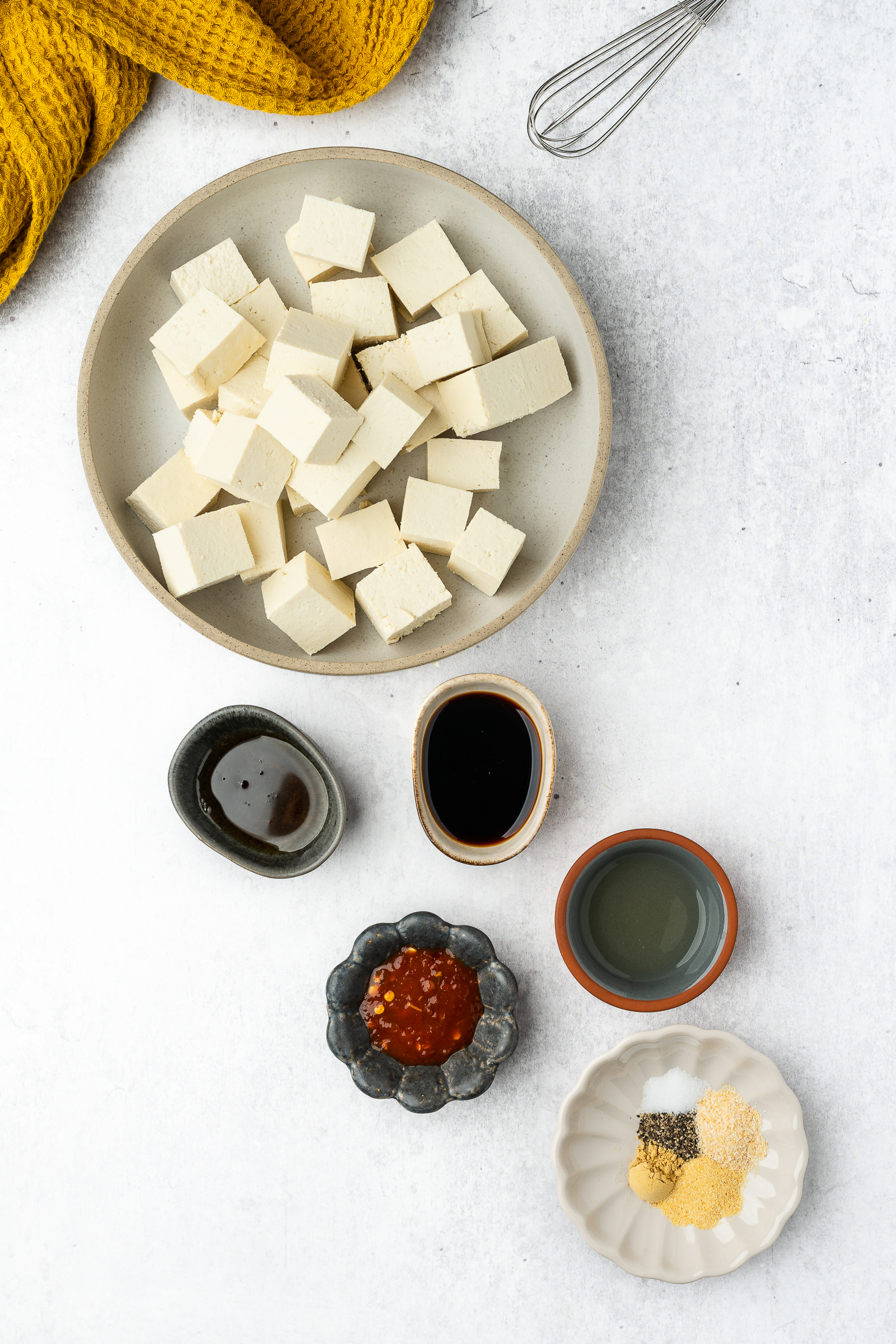 Cubed tofu in a shallow bowl with the marinade ingredients in small dishes.